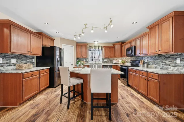 a kitchen with stainless steel appliances granite countertop a refrigerator a sink dishwasher a stove with wooden cabinets and wooden floor