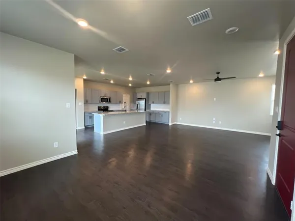 an empty room with wooden floor kitchen view and a kitchen