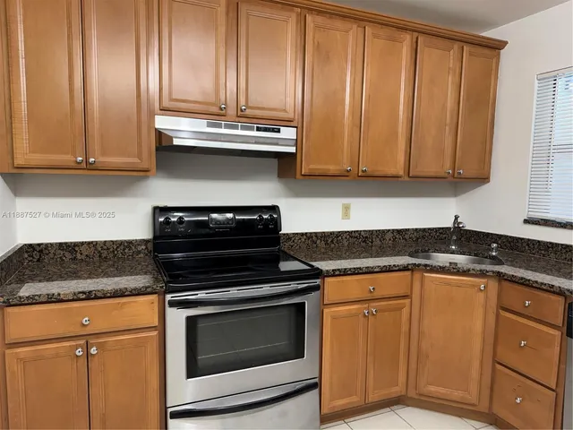 a kitchen with granite countertop wooden cabinets and a stove top oven