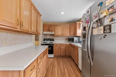 a kitchen with stainless steel appliances granite countertop a refrigerator a sink dishwasher a stove and white countertops with wooden floor