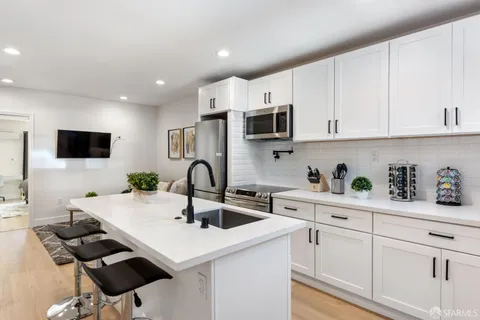 a kitchen with stainless steel appliances a sink a stove a microwave a refrigerator a cabinets and wooden floor