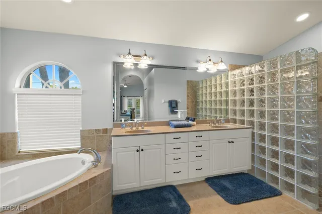 a bathroom with a double vanity sink a large mirror a bathtub and next to a window