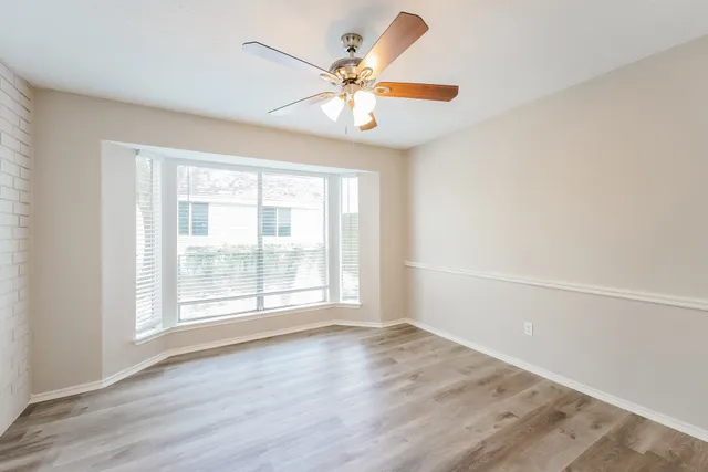 an empty room with wooden floor fan and windows