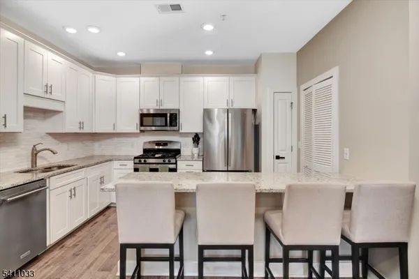 a kitchen with stainless steel appliances granite countertop a stove a sink a microwave a refrigerator with white cabinets and wooden floor