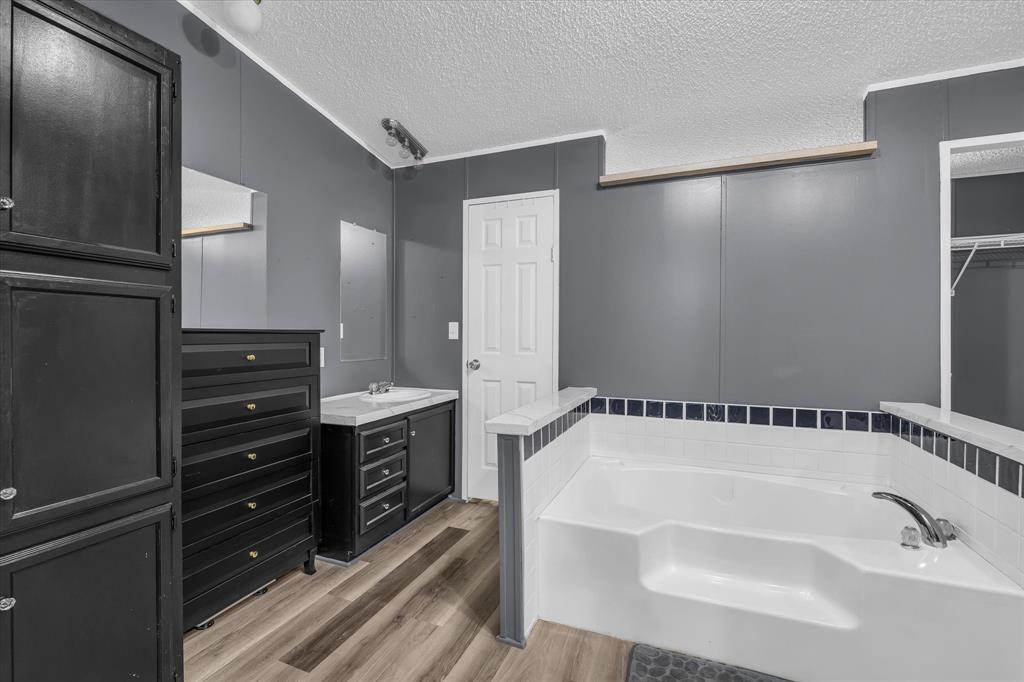 3615 Spring Valley Road Lorena, TX 76655 - Photo 22 of 33 Soaking tub with white and dark tile surround, single vanity with light countertop, and wood-finish flooring