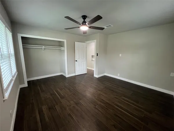 an empty room with wooden floor fan and windows