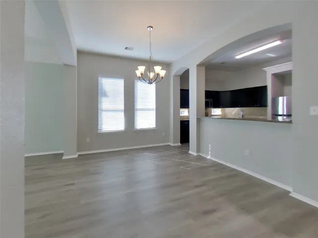a view of an empty room with window and kitchen view