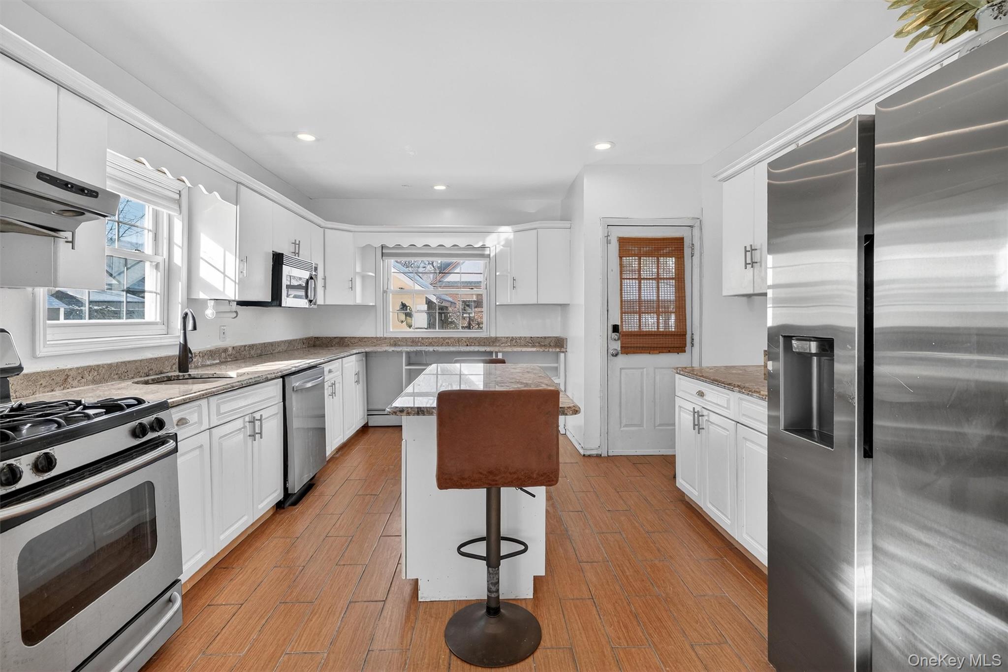 138-16 230th Street Queens, NY 11413 - Photo 11 of 49 1st floor kitchen with stainless steel appliances, white cabinetry, a center island, light stone countertops, and light wood-style floors