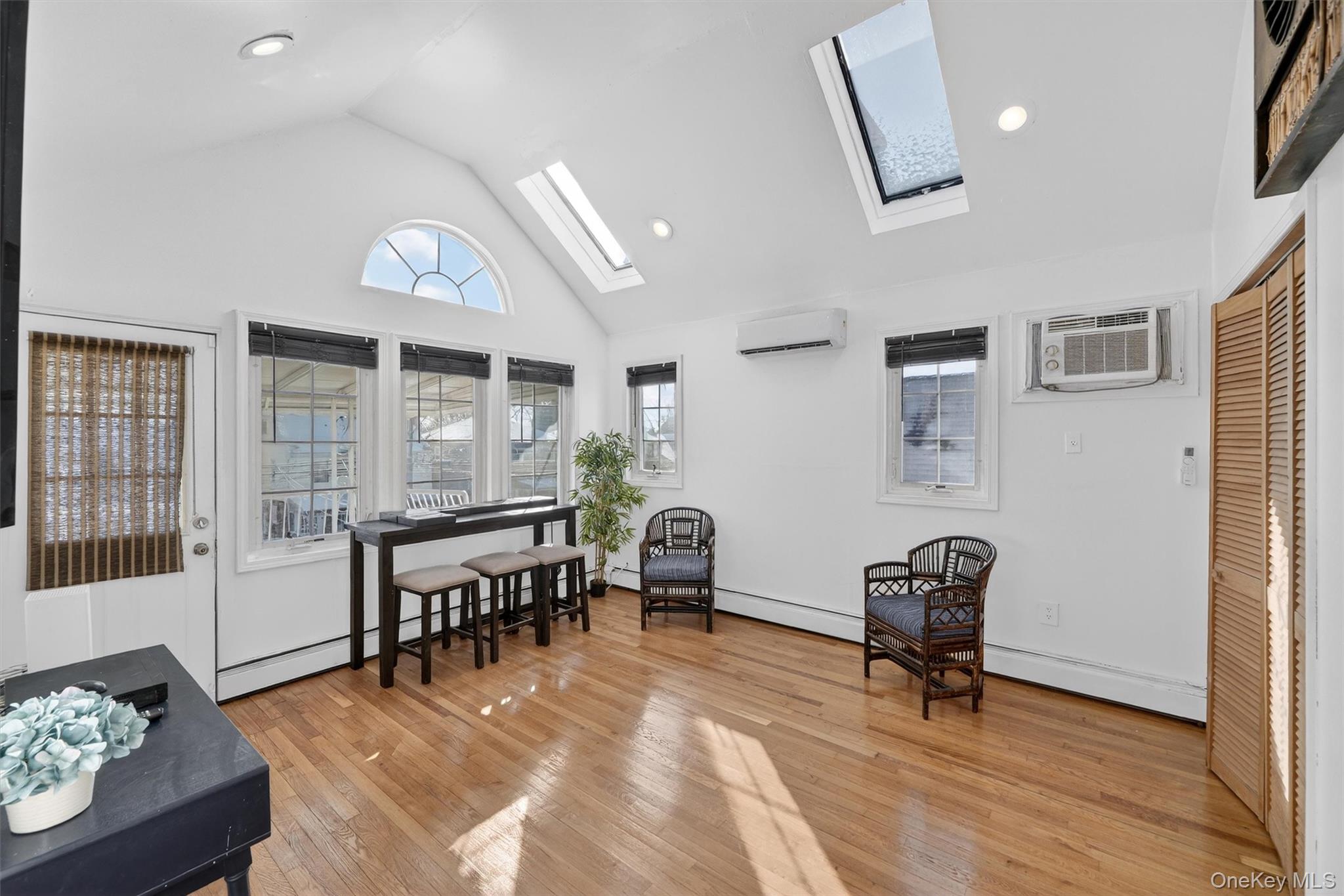 138-16 230th Street Queens, NY 11413 - Photo 24 of 49 Sitting room featuring high vaulted ceiling, a skylight, light wood-style flooring, baseboard heating, and a wall mounted AC (this is the 3rd bedroom)