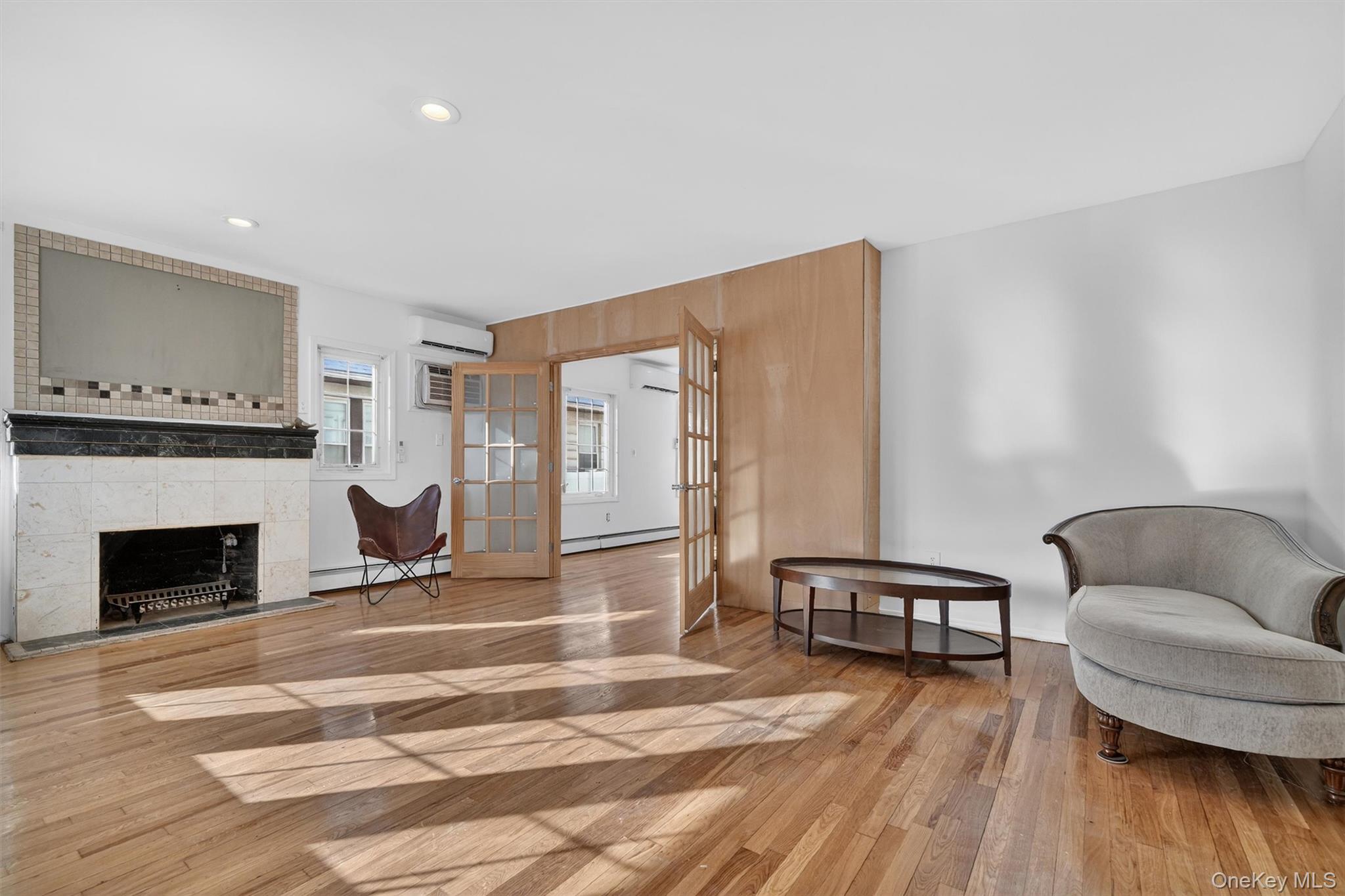 138-16 230th Street Queens, NY 11413 - Photo 3 of 49 Foyer featuring french doors, a tiled fireplace, baseboard heating, light wood-style floors, and a wall mounted air conditioner