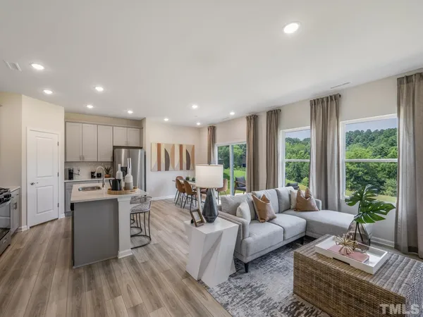a living room with stainless steel appliances furniture wooden floor and a kitchen view