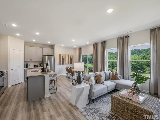 a living room with stainless steel appliances furniture wooden floor and a kitchen view