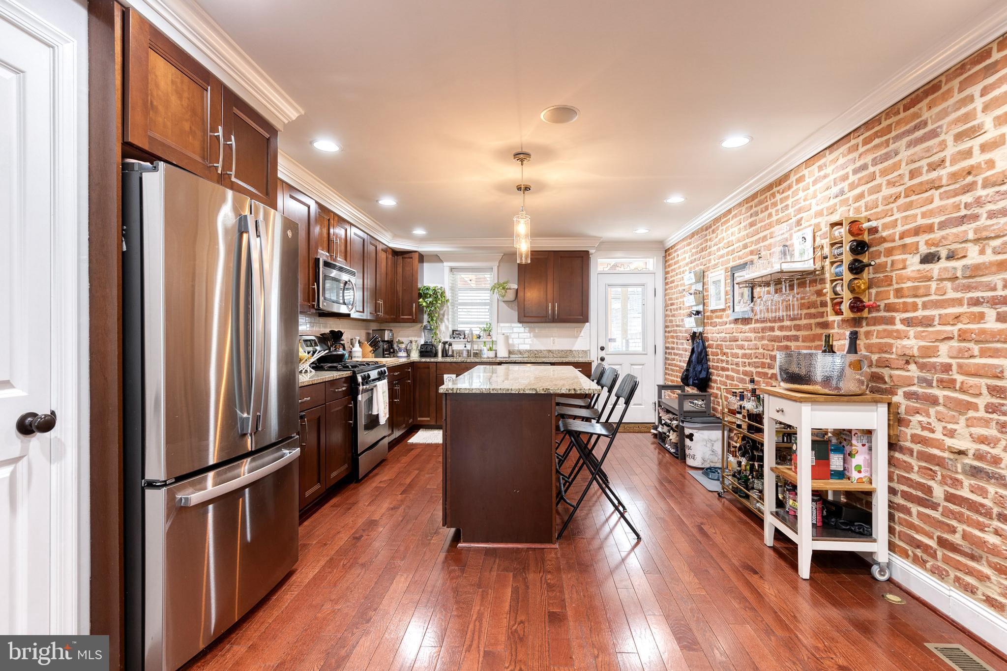 a kitchen with stainless steel appliances granite countertop a refrigerator oven a sink dishwasher and a dining table with wooden floor