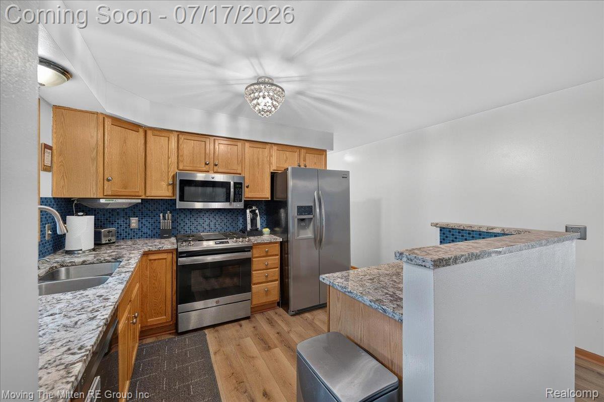 40162 Alden Road Belleville, MI 48111 - Photo 15 of 67 Kitchen featuring wood cabinetry, stainless steel appliances, speckled countertops, a blue mosaic tile backsplash, and wood-finish flooring
