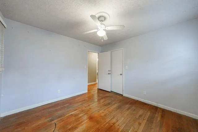 a view of an empty room with wooden floor and a ceiling fan