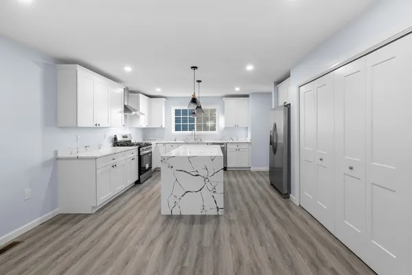 a kitchen with stainless steel appliances kitchen island granite countertop a refrigerator a sink dishwasher and white cabinets with wooden floor