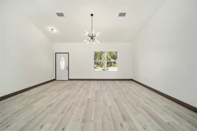 an empty room with wooden floor chandelier and windows