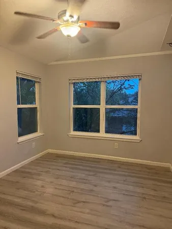 an empty room with wooden floor chandelier fan and windows