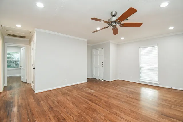 a view of an empty room with wooden floor and a ceiling fan