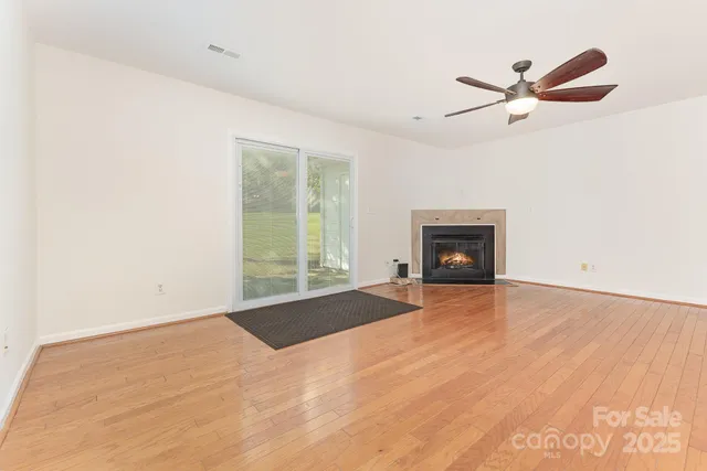 a view of a room with a fireplace a ceiling fan and wooden floor