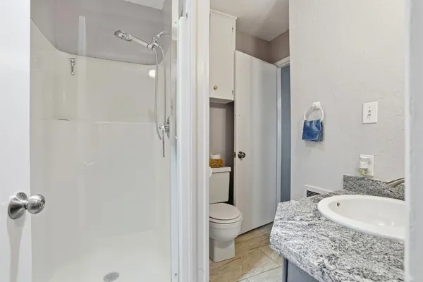 a bath room with a granite countertop sink a toilet and shower