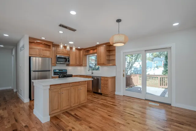 a kitchen with stainless steel appliances granite countertop a refrigerator a sink dishwasher a stove and a dining table with wooden floor