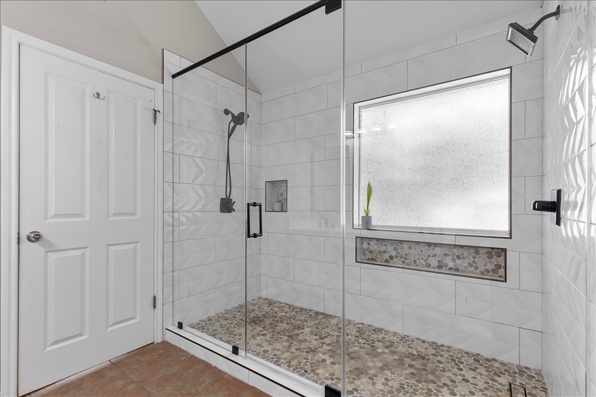 9012 Meacham Way Austin, TX 78749 - Photo 21 of 34 Walk-in shower featuring a frameless glass enclosure with matte black hardware, pebble tile flooring, white subway tile walls, a built-in shower niche with pebble tile accent, and a frosted privacy window