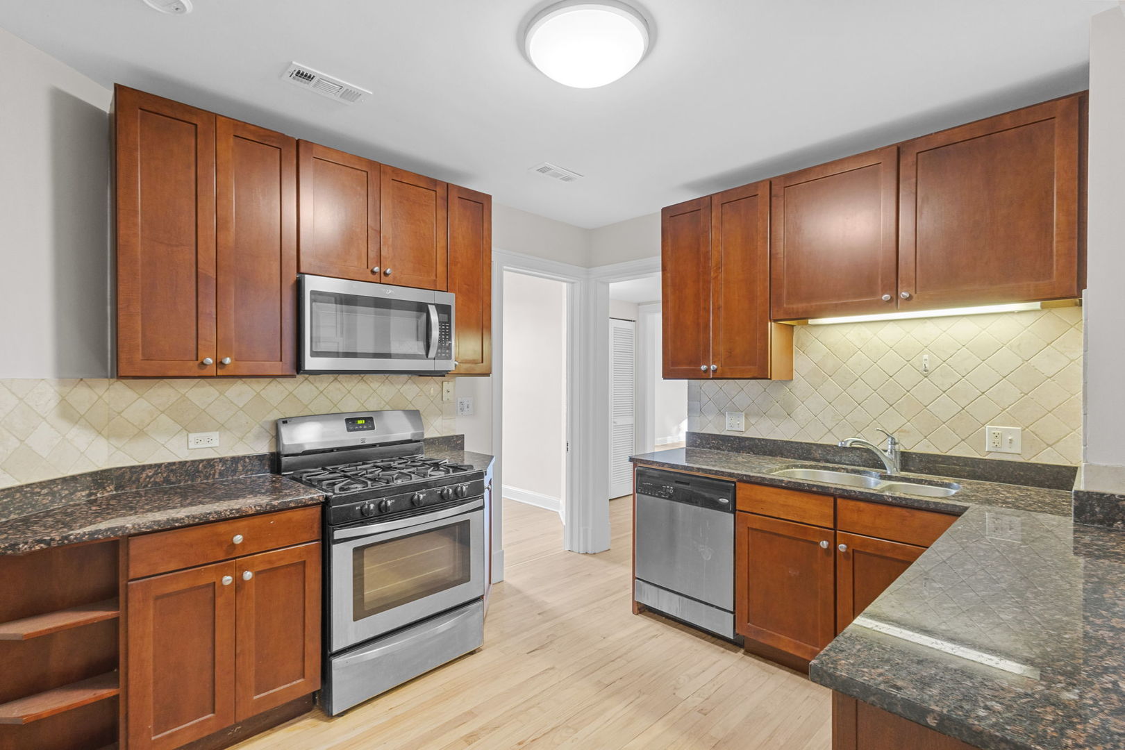 1014 West Roscoe Street, Unit 1F Chicago, IL 60657 - Photo 12 of 15 a kitchen with stainless steel appliances granite countertop wooden cabinets a stove top oven with wooden floor