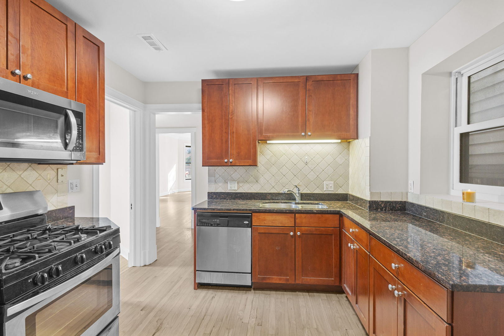 1014 West Roscoe Street, Unit 1F Chicago, IL 60657 - Photo 14 of 15 a kitchen with stainless steel appliances granite countertop wooden cabinets stove top oven and sink
