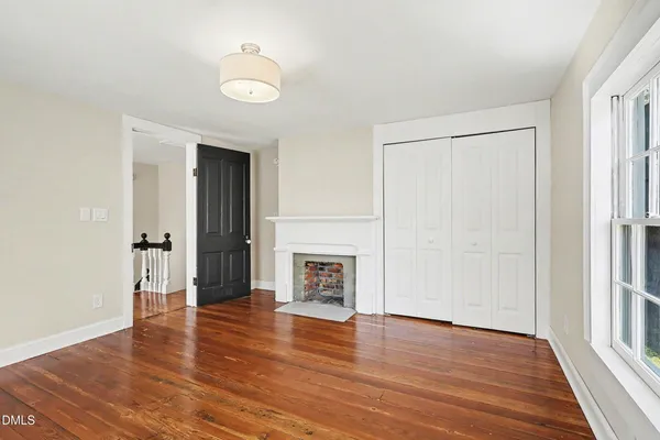 an empty room with wooden floor fireplace and windows