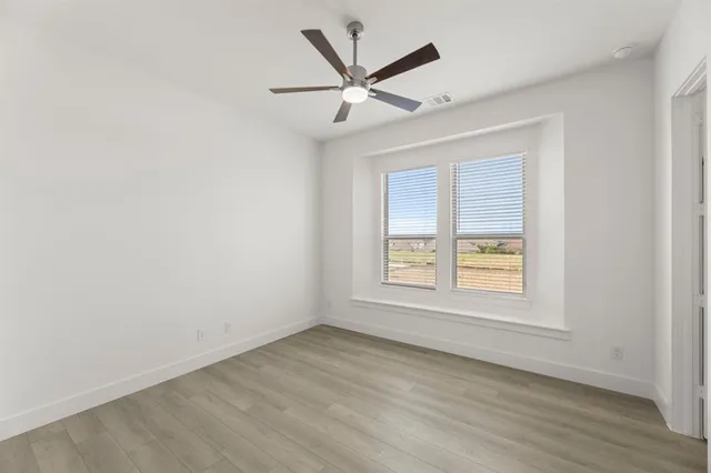 an empty room with wooden floor fan and windows