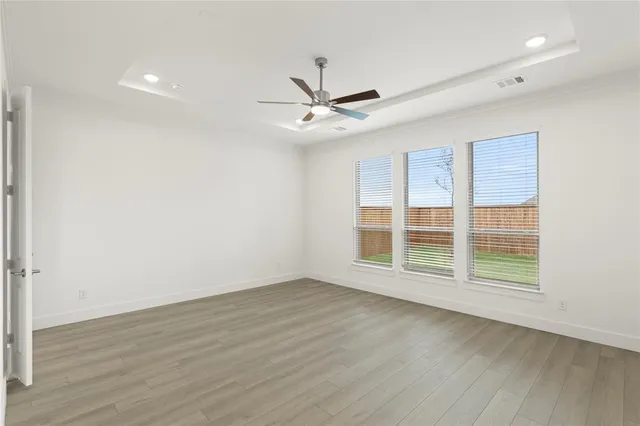 an empty room with wooden floor chandelier fan and windows