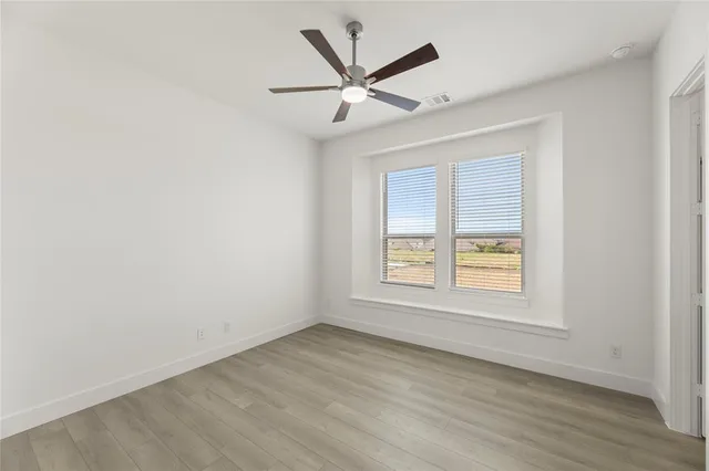 an empty room with wooden floor fan and windows