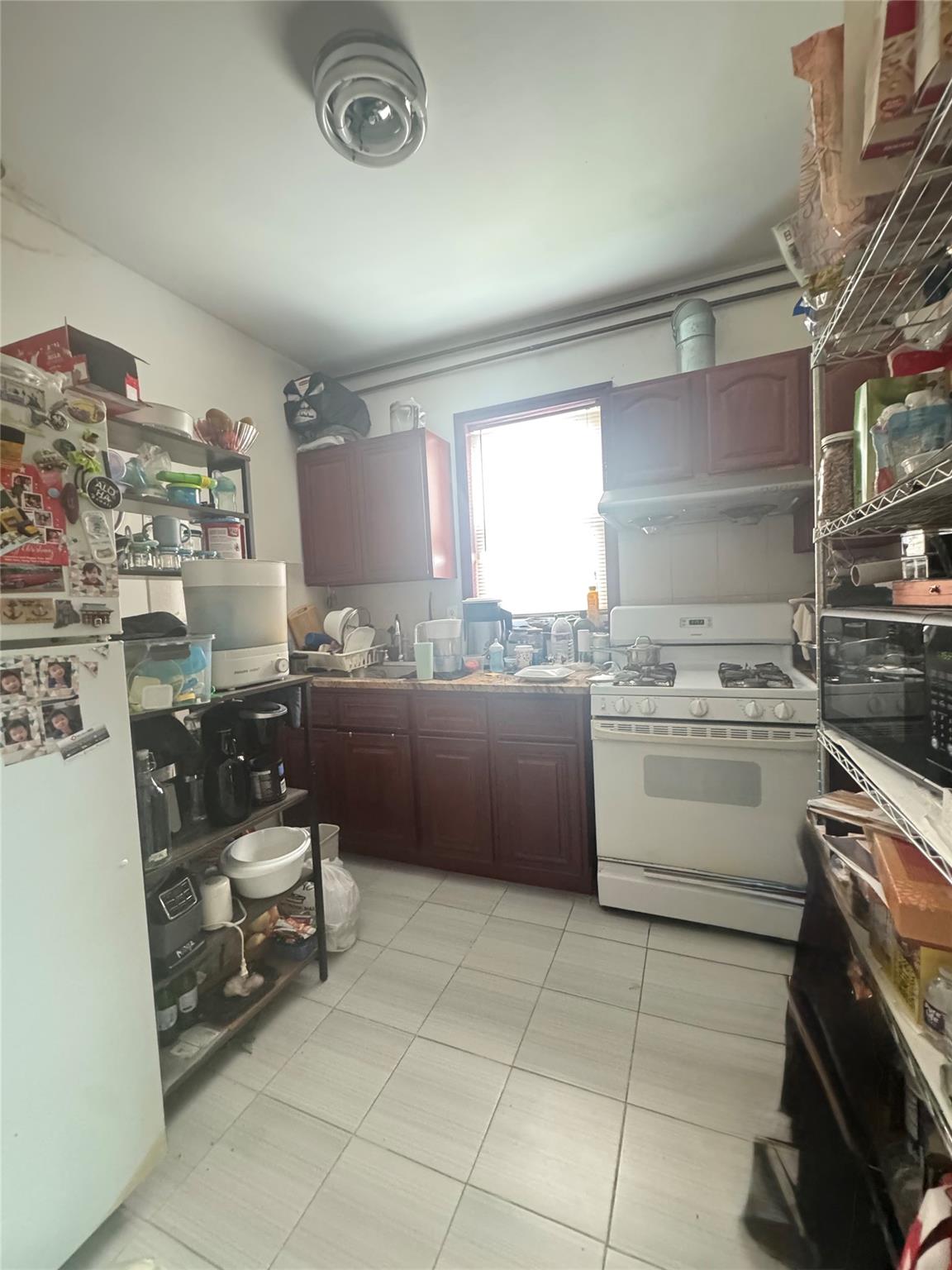 88-16 85th Street Queens, NY 11421 - Photo 9 of 11 Kitchen featuring white appliances, under cabinet range hood, and light tile patterned floors