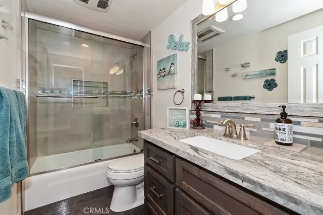 a bathroom with a granite countertop sink a toilet a mirror and shower
