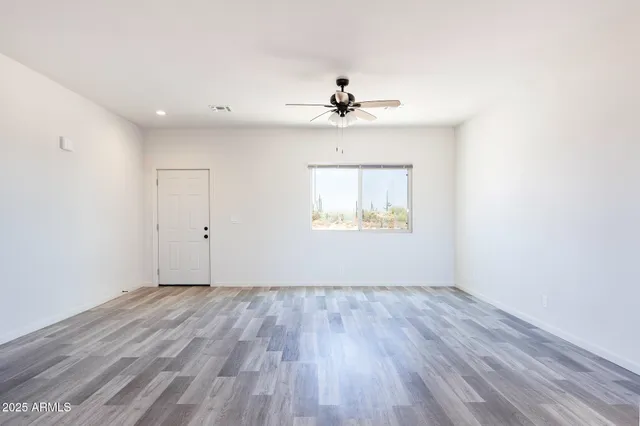 an empty room with wooden floor chandelier fan and windows