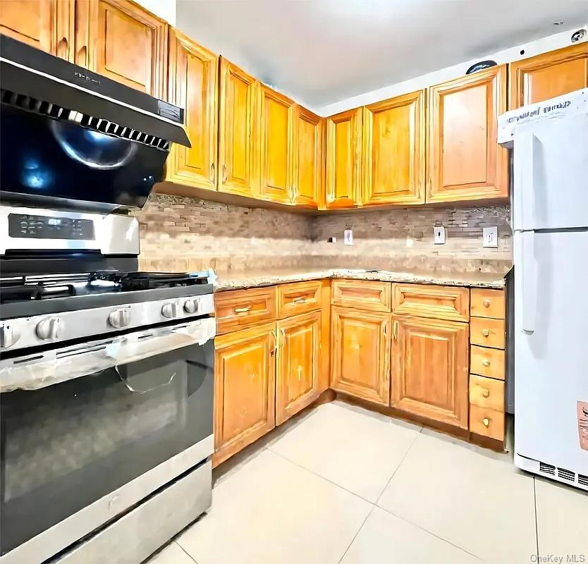 42-38 Judge Street, Unit 3A Queens, NY 11373 - Photo 4 of 9 Kitchen with stainless steel range with gas cooktop, freestanding refrigerator, exhaust hood, light tile patterned flooring, and decorative backsplash