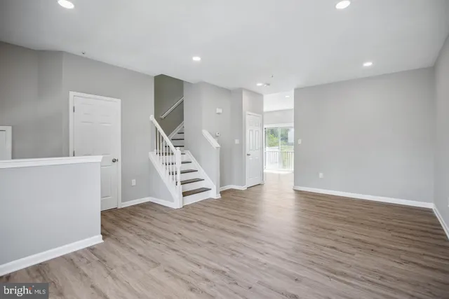 a view of an empty room with wooden floor stairs and a way to kitchen