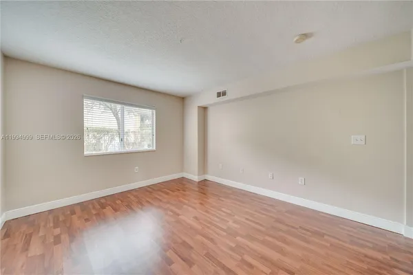 a view of an empty room with wooden floor and a window