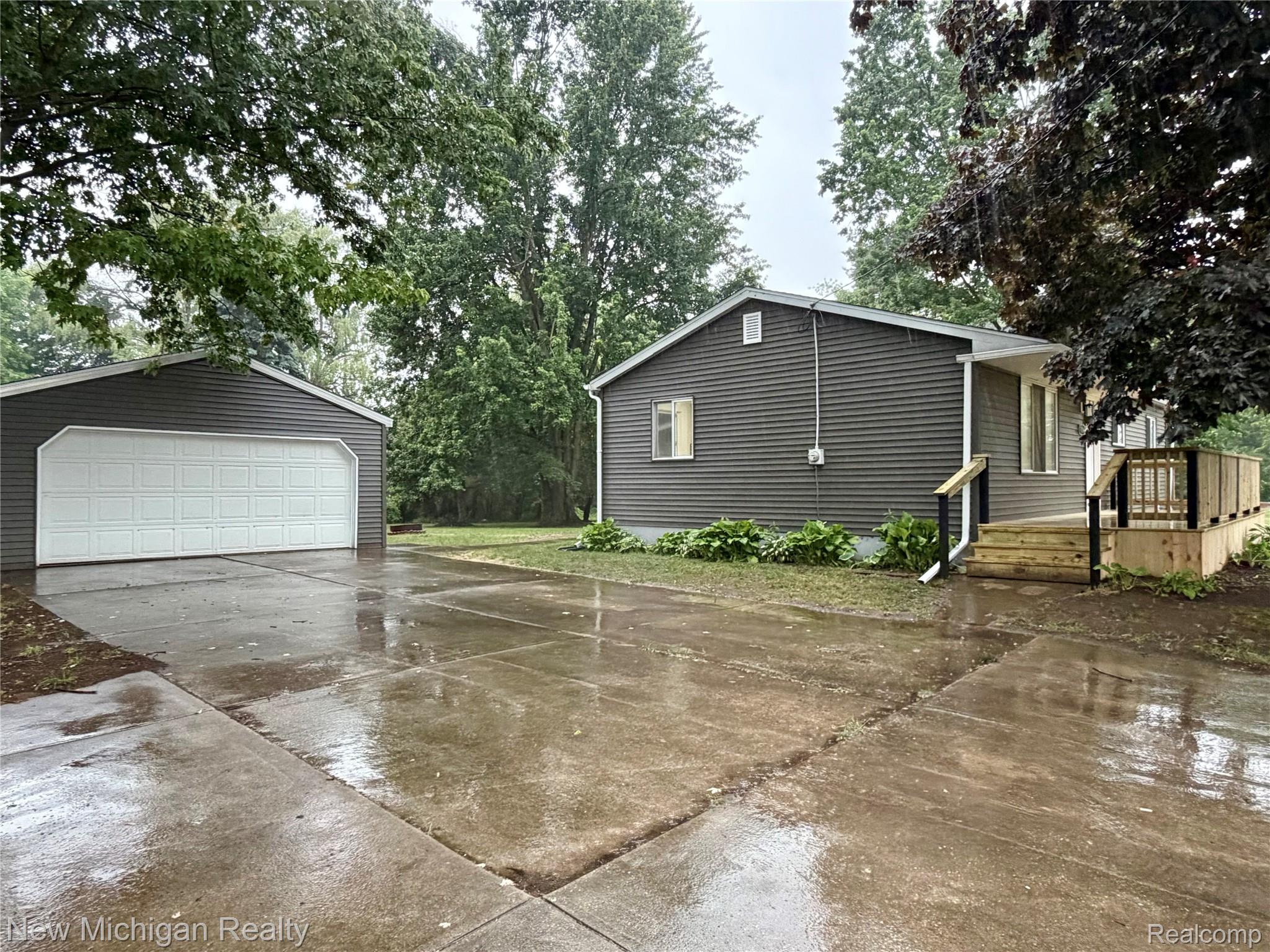 7104 Willard Road Millington, MI 48746 - Photo 5 of 30 Exterior featuring gray horizontal siding, a newly constructed wooden deck with black railings, and a concrete driveway