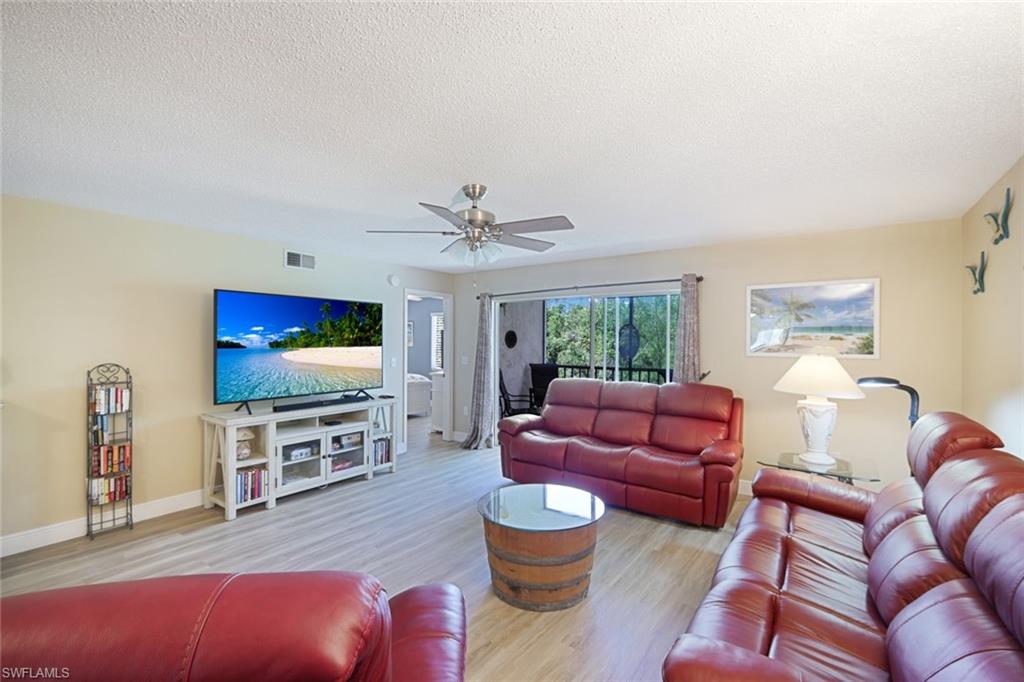 3041 Sandpiper Bay Circle, Unit H203 Naples, FL 34112 - Photo 8 of 23 a living room with furniture a flat screen tv and a large window