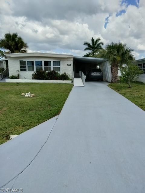 View of front of house featuring concrete driveway, an attached carport, and a front lawn