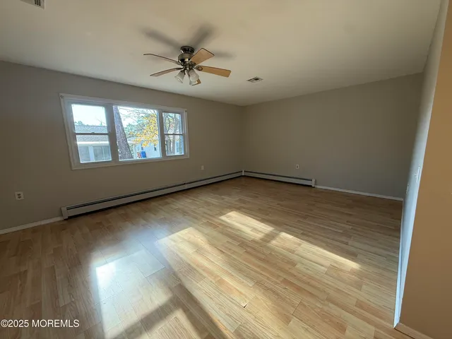 an empty room with wooden floor fan and windows