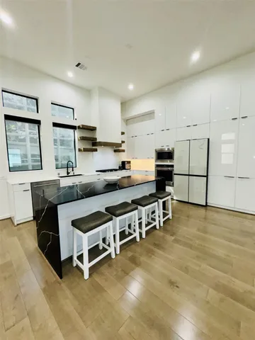 a kitchen with stainless steel appliances kitchen island granite countertop a stove a refrigerator a sink a dining table and chairs with wooden floor
