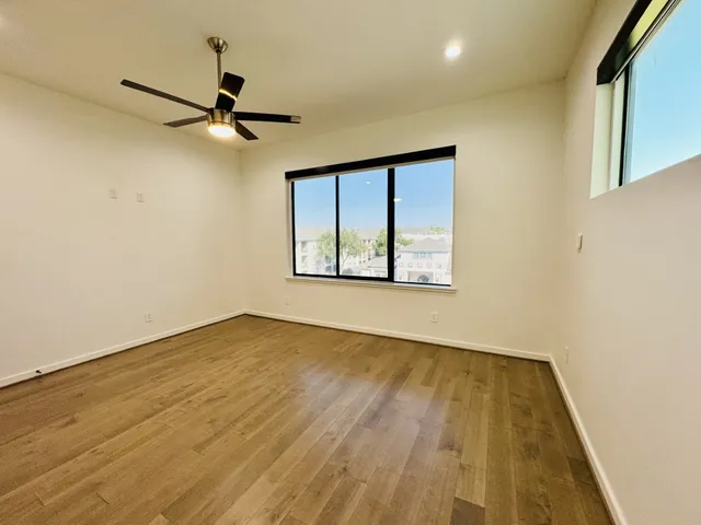 an empty room with wooden floor fan and windows