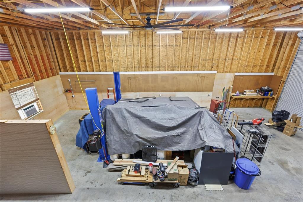 110 Highview Road Ennis, TX 75119 - Photo 33 of 40 Spacious interior featuring exposed wood framing, high ceilings, multiple fluorescent light fixtures, and a large roll-up garage door
