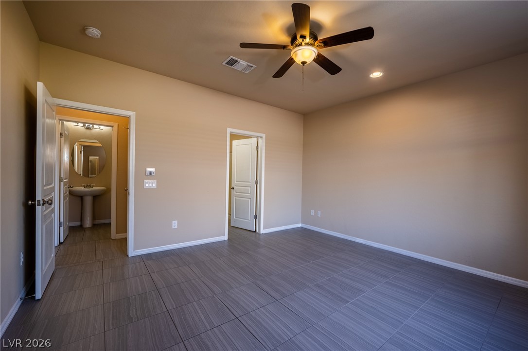 11016 Prairie Grove Road Las Vegas, NV 89179 - Photo 13 of 37 A spacious room features clean tiled floors and a ceiling fan, with a glimpse into a bathroom.