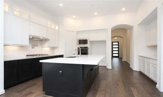 a kitchen with stainless steel appliances a sink dishwasher a stove and white cabinets with wooden floor