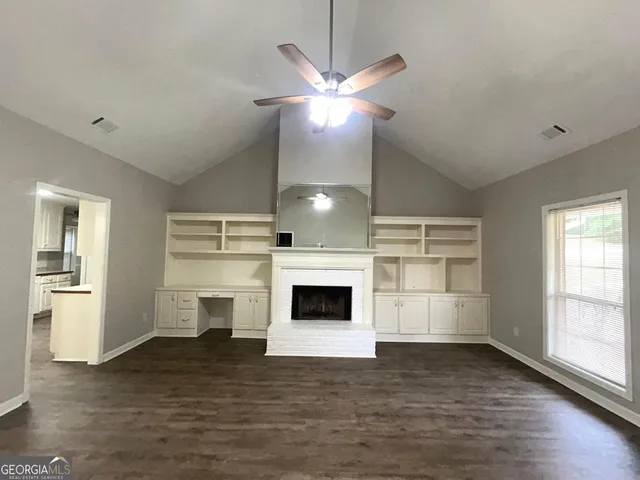 a view of a livingroom with a fireplace a ceiling fan and windows