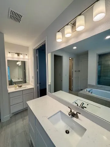 a bathroom with a sink vanity granite tub and a mirror